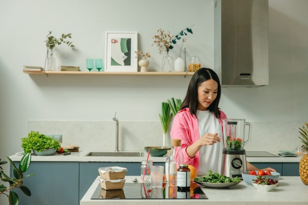 A woman in the kitchen putting vegetables into a blender