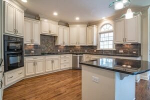 Modern kitchen with light-colored cabinetry, granite countertops, stainless steel appliances, and hardwood flooring.