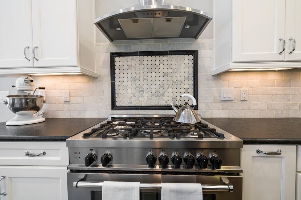 Metal stove, black kitchen counter, white cabinets, kettle, mixer
